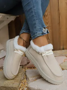 Close-up view of beige fur-lined winter snow boots with white laces on stone ground.