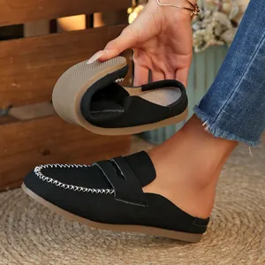 Detail view of highly flexible black suede flat mules with white decorative stitching.
