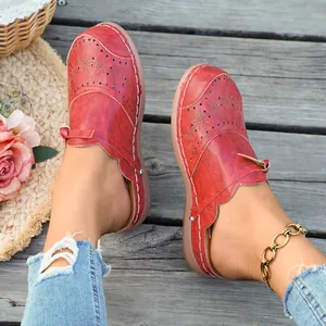 Detailed shot of red retro wedge mules featuring decorative floral cutouts and stitching