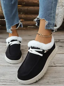 Close-up of black fur-lined snow boots with white laces on a wooden floor