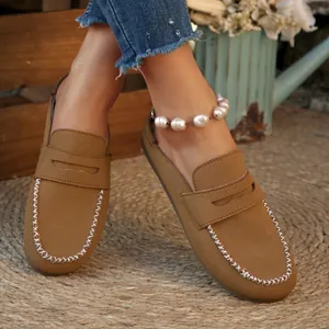 Detail view of tan suede mules loafers with stylish white contrast stitching on a rug.