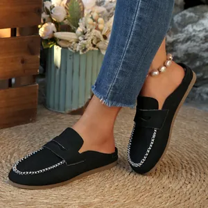 Detail view of stylish black suede flat mules with white contrast stitching on a straw mat