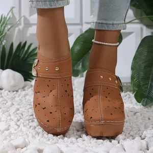 Detail of brown hollow-out platform mules with metal buckle on white pebbles