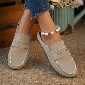 Close-up detail of beige suede backless loafers featuring elegant white stitching and flat sole