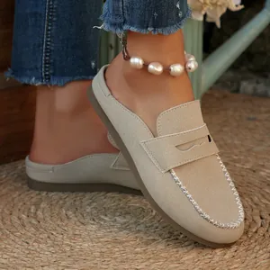 Close-up view of beige suede backless loafers featuring decorative white stitching details.