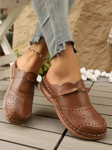 Close-up of brown vintage wedge clogs with floral laser-cut patterns and white stitching