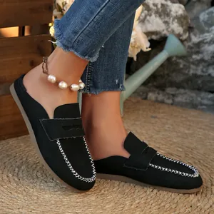 Detail view of black suede flat mules featuring white decorative stitching in a garden setting