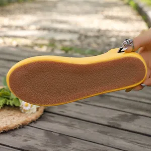 Detailweergave van de duurzame antislip rubberen zool van een gele platte zomersandaal.