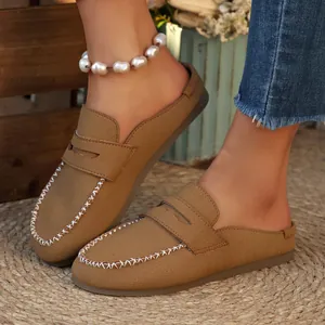 Close-up of brown suede backless loafer mules featuring white decorative stitching