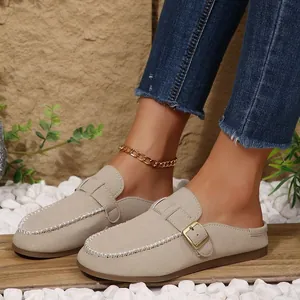 Detail view of beige suede closed-toe mules with buckled strap and white stitching.