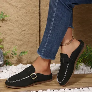Close-up of black closed-toe flat mule slippers with white stitching and buckle detail