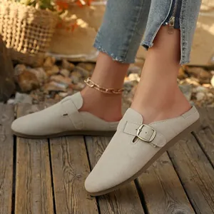 Beige suede round toe flat backless loafers with metal buckle detail on wooden floor
