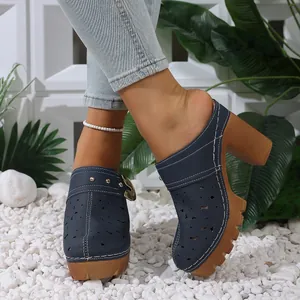 Close-up of navy blue laser-cut heeled mules with chunky wooden-style soles on pebbles