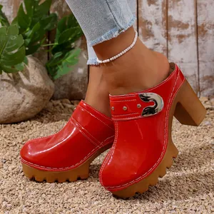 Red patent leather clogs with thick high heels and a decorative metallic buckle detail
