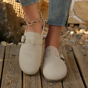 Close-up of beige suede flat mules with buckle strap on a wooden deck