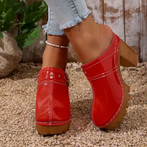 Detail view of red patent leather platform clogs with chunky high heels and rivet accents