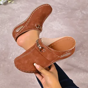 Detailed macro view of brown suede wedge clogs featuring metallic chain and white stitching