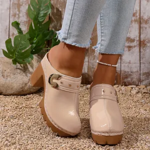 Detail view of stylish beige patent leather clogs featuring chunky high heels and gold rivets.