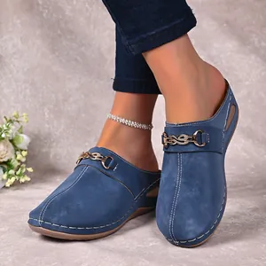 Stylish blue wedge mules with metal buckle detail worn with jeans on textured background