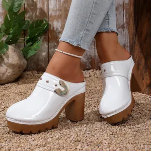 Macro detail of white patent leather chunky heel mules with gold buckle and rivets