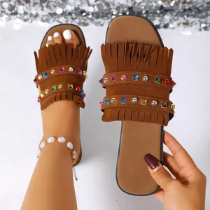 Close-up detail of brown suede flat sandals featuring colorful studs and stylish fringe decoration.