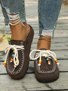 Detalle de los zuecos de ante marrón con cuentas de colores y cordones de cuerda de algodón
