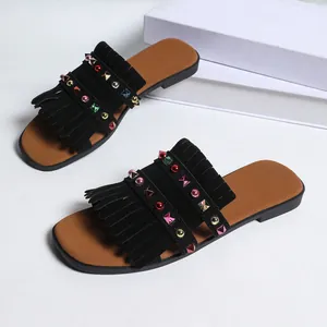 Close-up detail of women's flat slides featuring black suede fringe and colorful rhinestones.