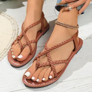 Detail view of stylish brown braided strap flat thong sandals for women on white floor.