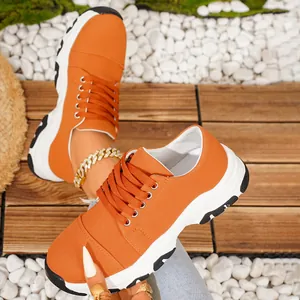 Close-up of vibrant orange thick-sole sneakers on rustic wooden deck and pebbles.