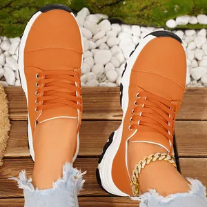 Detail of orange thick-soled sneakers for women styled with frayed denim and anklet