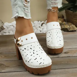 Close-up of white laser-cut floral clogs with chunky brown heels and gold buckles
