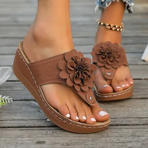 Macro detail of brown wedge thong sandals with large 3D flower and white stitching