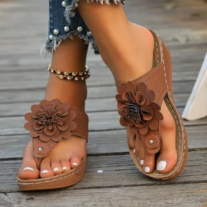 Close-up of brown wedge thong sandals with 3D flower decoration on wooden background