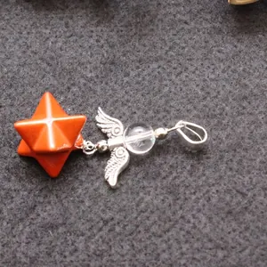 Angel wing pendant with red Merkaba star and clear crystal bead on grey background.