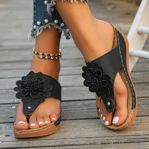 Close-up detail of black wedge flip-flop sandals featuring an oversized floral decoration