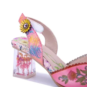 Detalle de sandalia retro de cuero floral con tacón transparente y flores secas.