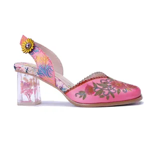 Detalle de sandalias retro de cuero rosa hechas a mano con bordado floral y tacón transparente.