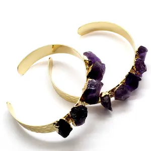A pair of gold hammered cuff bracelets featuring irregular raw purple amethyst stones
