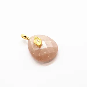 Macro view showing detail of faceted pink sunstone pendant with gold evil eye charm