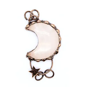 Primer plano de un colgante de luna de cobre vintage con piedra rosa y dije de estrella