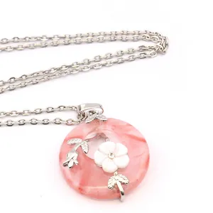 Close-up of pink crystal donut pendant with white flower ornament and silver leaf details