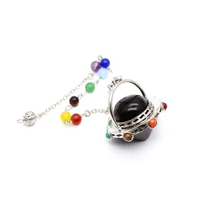 Detalle de un péndulo de cristal con forma de OVNI y cuentas de chakra de colores.