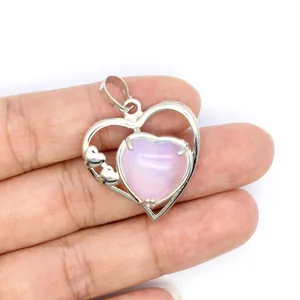 Gros plan d'un pendentif cœur en argent avec pierre rose tenu à la hand pour l'échelle