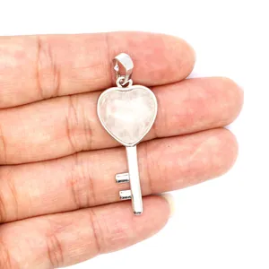 Detailed view of a natural pink crystal heart key pendant held in hand for scale.