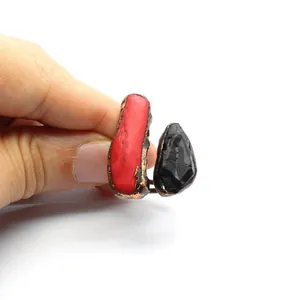 Detail shot of hand holding a raw red and black stone open ring with bronze finish.