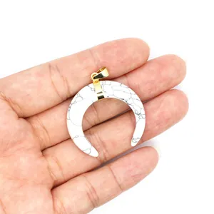 Detailed view of a white marble texture horn pendant with gold bail held in hand