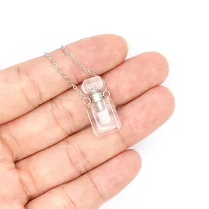 Détail d'un collier pendentif mini flacon de parfum en cristal tenu délicatement dans la main