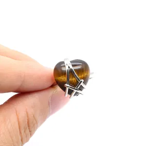Close-up of a heart-shaped tiger's eye gemstone ring held by a hand on a white background