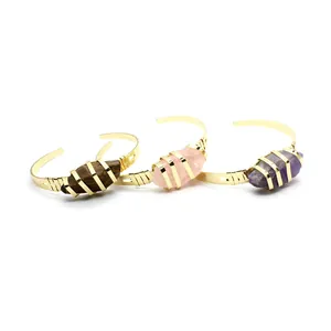 Dettaglio di tre bracciali placcati oro con pietre naturali grezze come l'ametista.