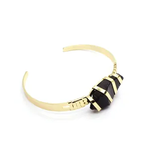 Vista dettagliata di un bracciale rigido placcato oro con pietra nera grezza avvolta.